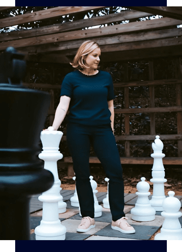 A woman standing in front of some chess pieces.