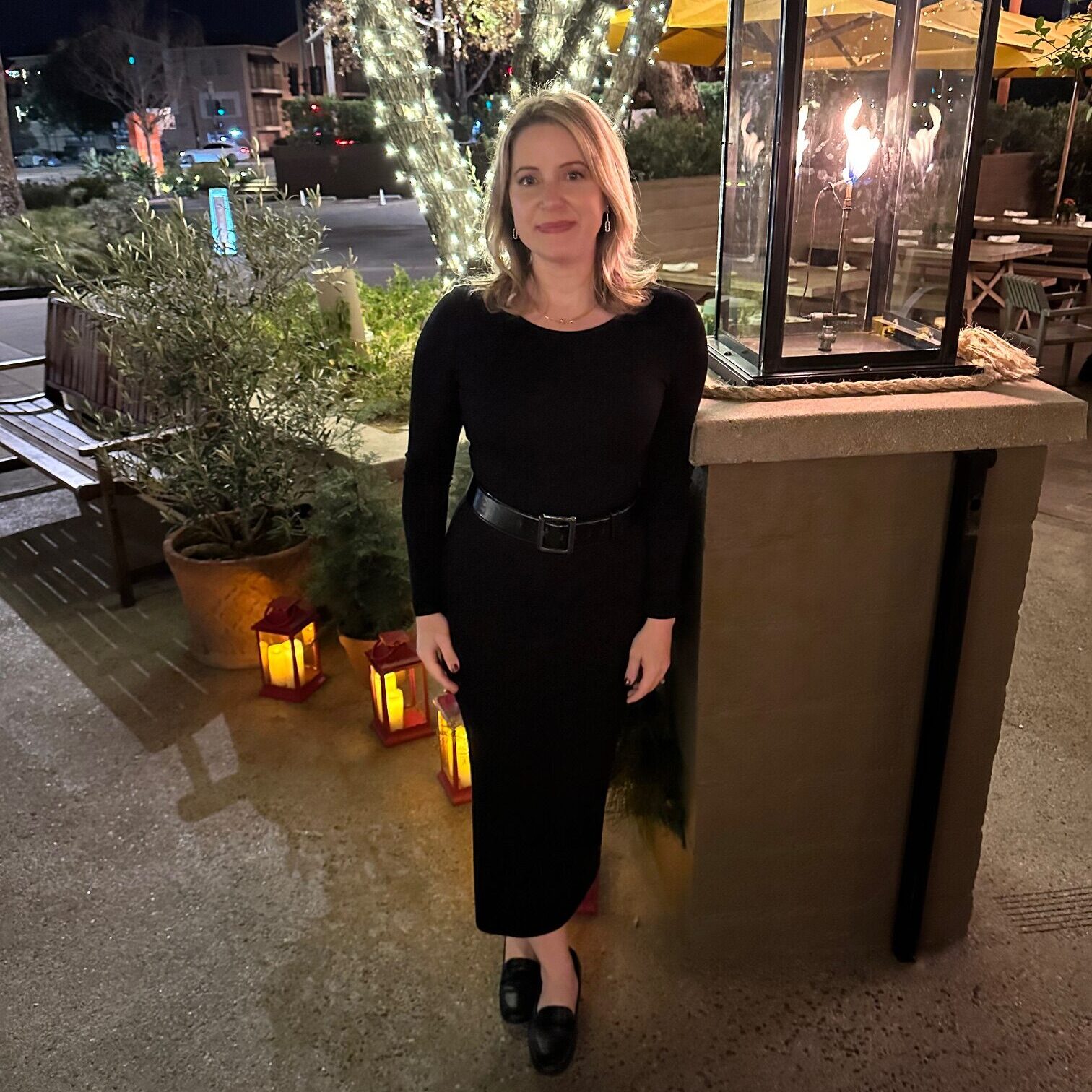 A woman in black dress standing next to a pillar.